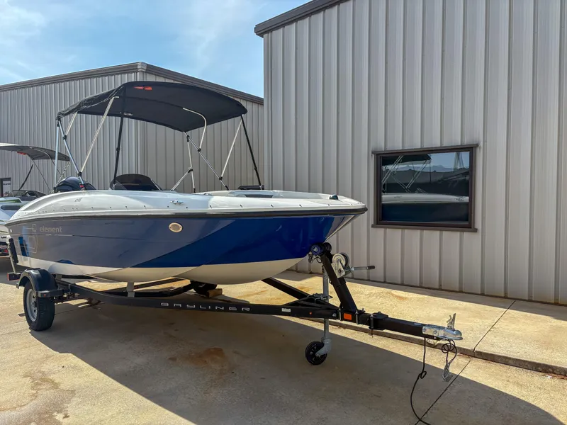 Slide: The Image of 2019 Bayliner Element E16 boat on trailer, parked near metal building. - 2
