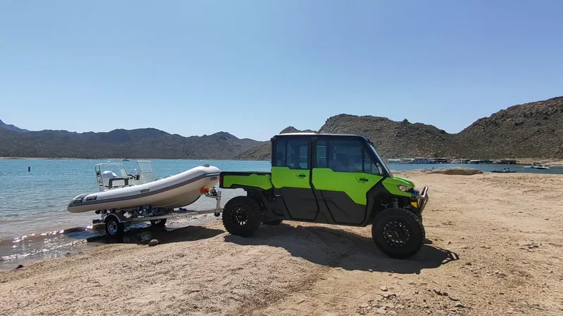 Slide: The Image of 2025 Tide Craft Catalina 13 DEMO Boat on trailer, parked by a scenic lakeside with rugged terrain. - 7