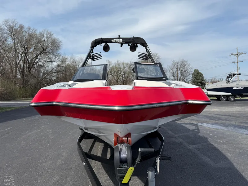 Slide: The Image of 2020 Axis A24 boat with red and white hull on a trailer, parked outdoors. - 2