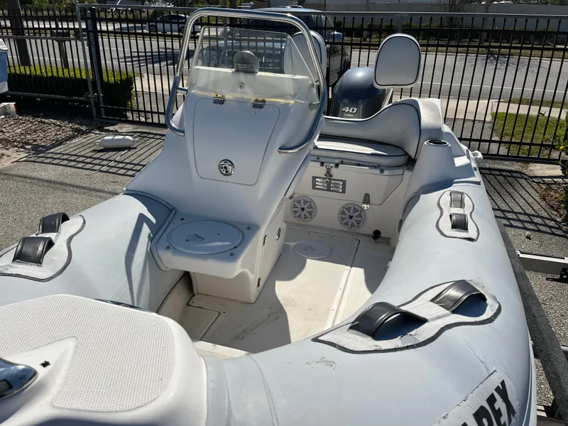 Slide: The Image of 2014 Apex A-11 Tender boat with seating, steering console, and storage, parked near a fence. - 9