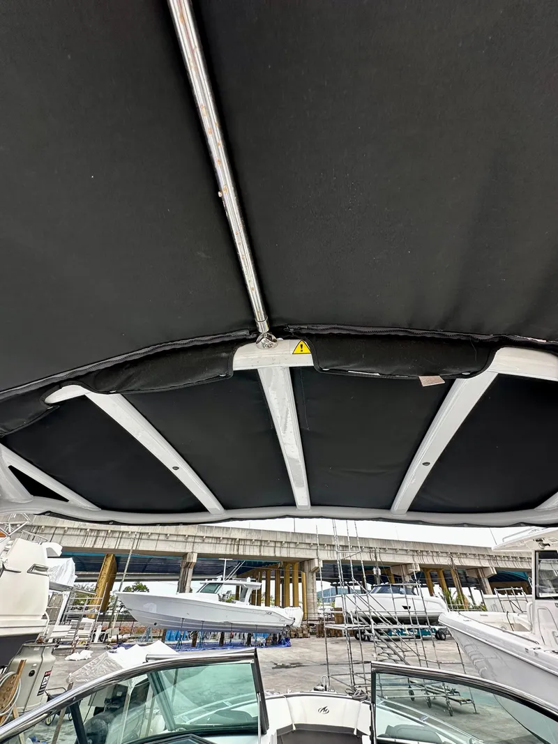 Slide: The Image of 2022 Monterey 275 Super Sport boat with black canopy, docked near a marina. - 14