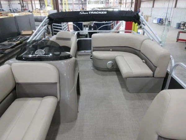 Slide: The Image of 2023 Sun Tracker Party Barge 18 DLX interior with beige seating and helm in a warehouse. - 6