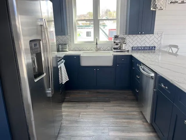 Slide: The Image of Modern kitchen with navy cabinets, stainless steel appliances, farmhouse sink, and chevron backsplash in Harbor Cottage. - 11