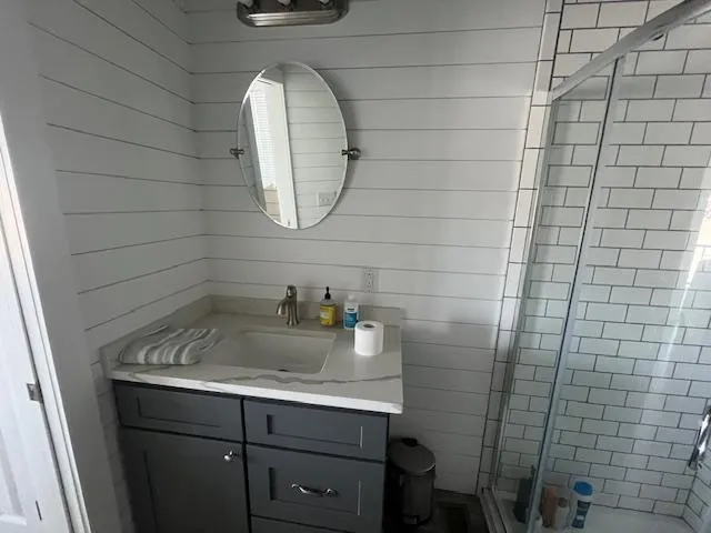 Slide: The Image of Modern bathroom with gray vanity, oval mirror, and glass shower in Harbor Cottage 16 x 84 model. - 31