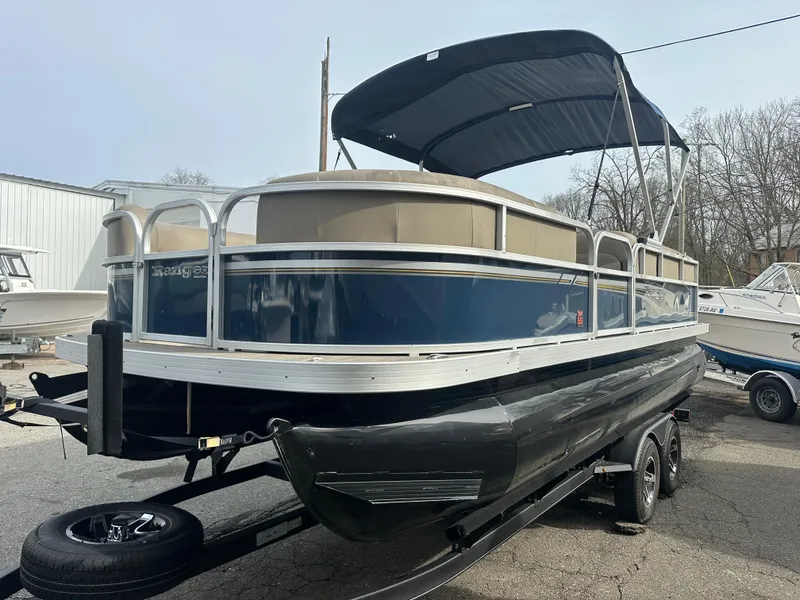 Slide: The Image of 2023 Ranger Reata 200C pontoon boat with canopy on trailer, parked outdoors. - 1