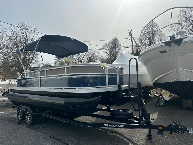 Slide: The Image of 2023 Ranger Reata 200C pontoon boat on trailer, parked outdoors with cover and canopy. - 3