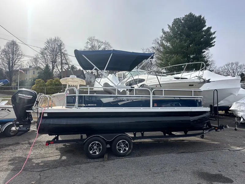 Slide: The Image of 2023 Ranger Reata 200C pontoon boat on trailer, parked outdoors with other boats. - 4