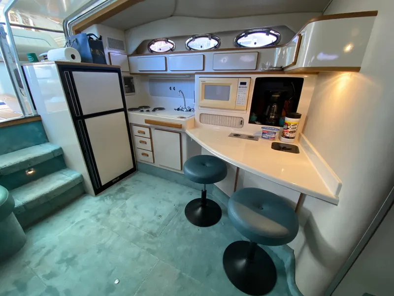 Slide: The Image of 1995 Sea Ray 400 Express Cruiser kitchen with bar stools, microwave, and refrigerator. - 16