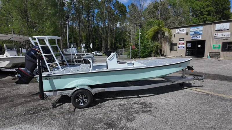 Slide: The Image of 2025 Xpress Skiff 185 boat on trailer, parked outdoors near a building. - 10