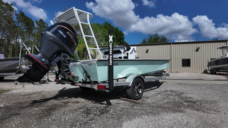 Slide: The Image of 2025 Xpress Skiff 185 boat on trailer, parked outdoors under blue sky. - 15