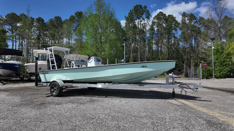 Slide: The Image of 2025 Xpress Skiff 185 boat on trailer, parked outdoors with trees in background. - 3