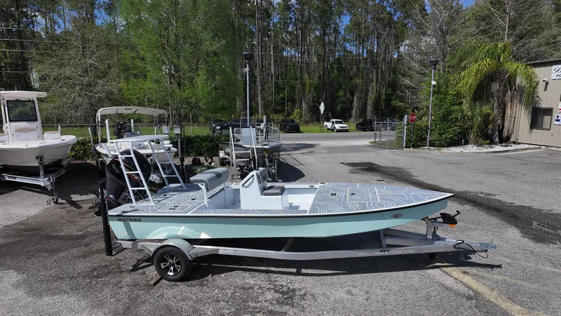 Slide: The Image of 2025 Xpress Skiff 185 boat on trailer, parked outdoors with trees in the background. - 8