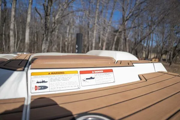 Slide: The Image of 2017 Correct Craft Super Air Nautique GS boat deck with warning labels, surrounded by trees. - 29