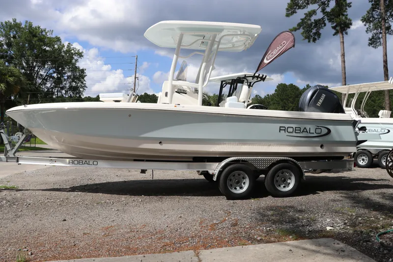 Slide: The Image of 2025 Robalo 226 Cayman boat on trailer, parked outdoors under cloudy sky. - 2