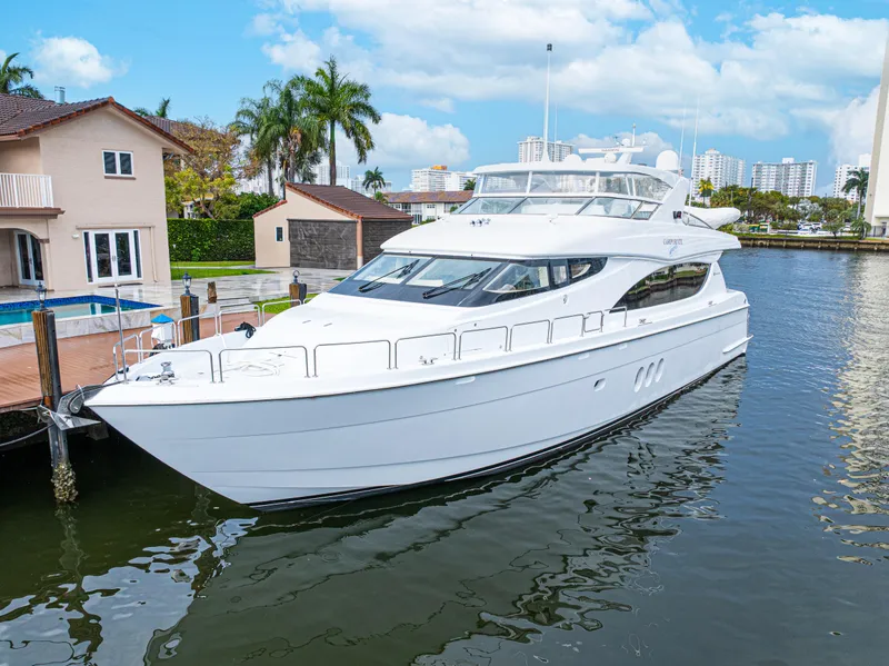 The Image of 2005 Hatteras 80 Motor Yacht docked by waterfront homes under a blue sky. - 1