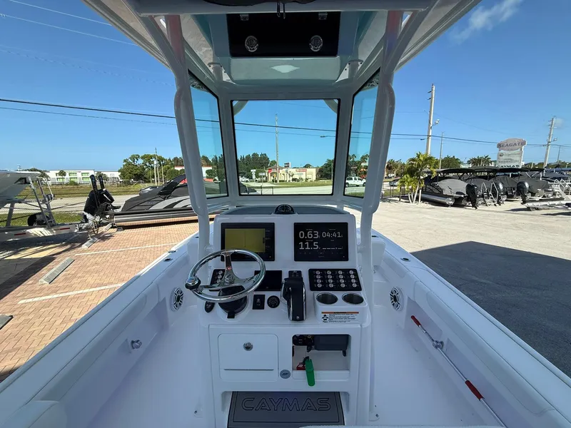 Slide: The Image of 2024 Caymas 26 HB boat cockpit with steering wheel and control panel, docked outdoors. - 11