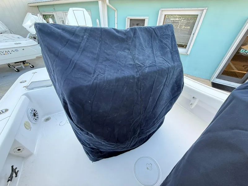 Slide: The Image of 2024 Caymas 26 HB boat interior with covered equipment, white deck, and blue building background. - 17