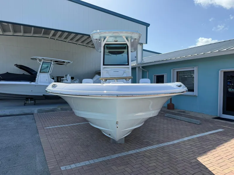 Slide: The Image of 2024 Caymas 26 HB boat displayed outdoors, front view, near a blue building. - 2