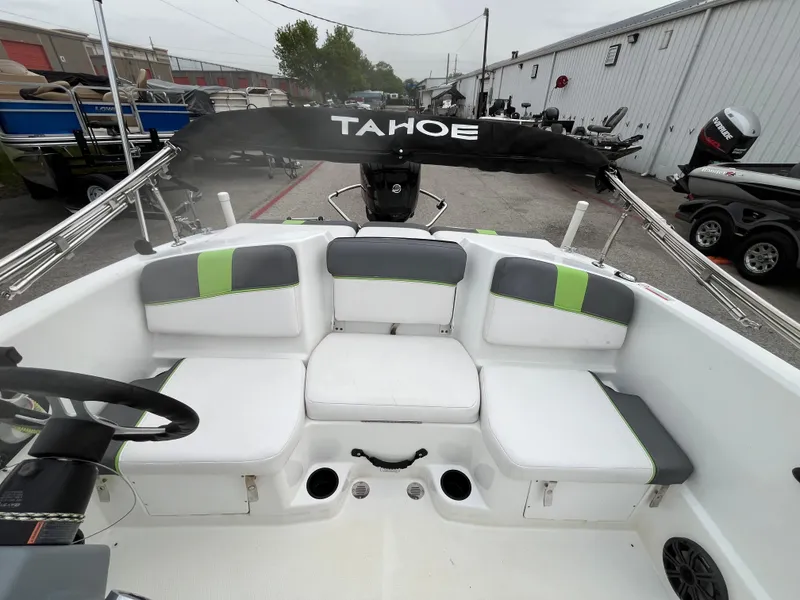 Slide: The Image of 2021 Tahoe T16 boat interior with cushioned seating and steering wheel, docked outdoors. - 21