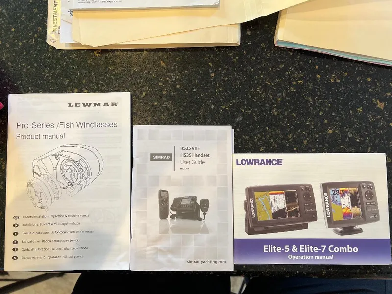 Slide: The Image of Manuals for Lewmar windlasses, Simrad VHF, and Lowrance Elite fish finders on a table. - 6
