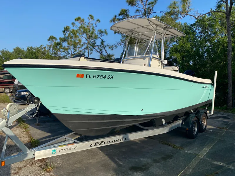 Slide: The Image of 2021 Cobia 237 Center Console boat on trailer, light blue hull, parked outdoors. - 37