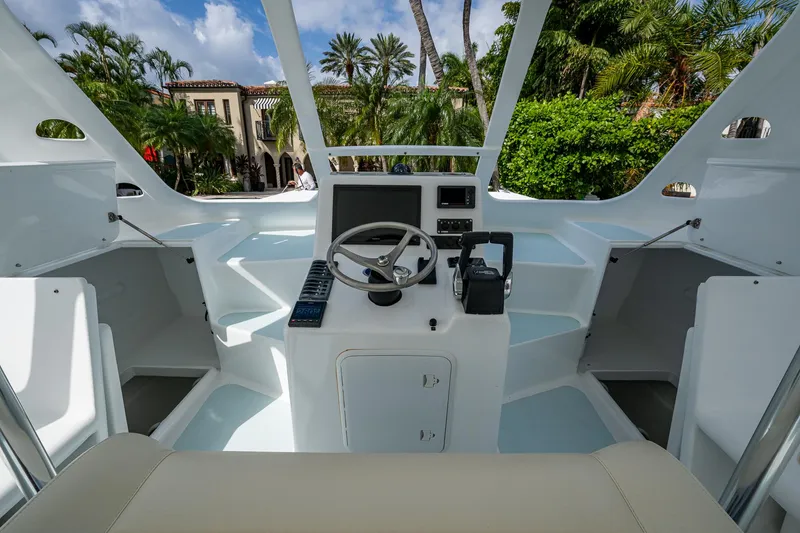 Slide: The Image of Cockpit of 2019 Aventura 31 Cat boat with steering wheel and controls, surrounded by lush greenery. - 4