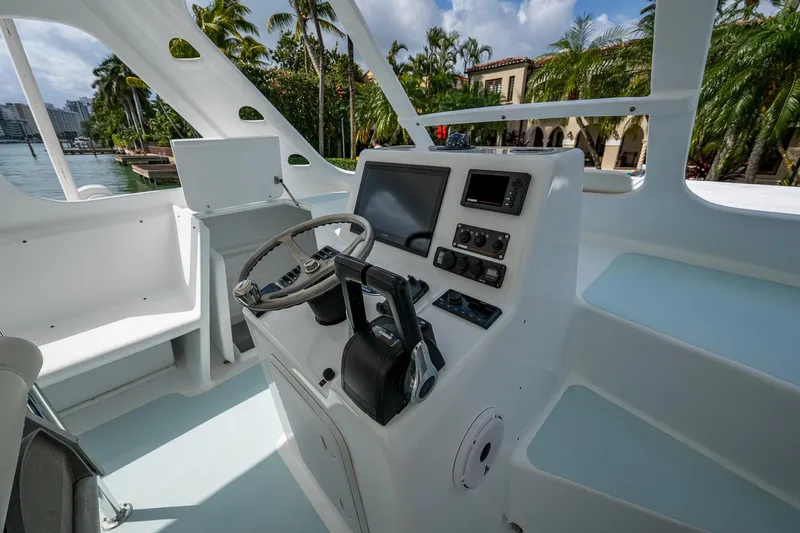 Slide: The Image of 2019 Aventura 31 Cat boat cockpit with steering wheel and control panel, surrounded by tropical scenery. - 5