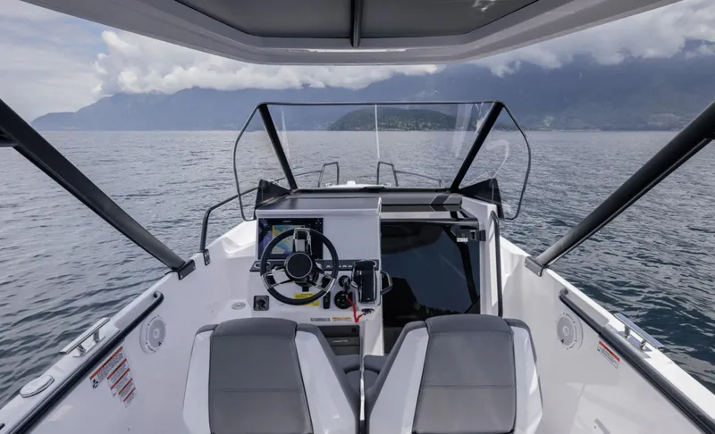 Slide: The Image of 2025 Axopar 25 Cross Top boat interior with steering wheel, on calm water, mountainous backdrop. - 4