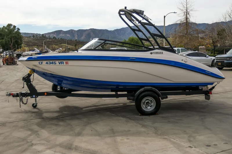 Slide: The Image of 2019 Yamaha AR 190 boat on trailer, blue and white, parked outdoors with mountains in background. - 9