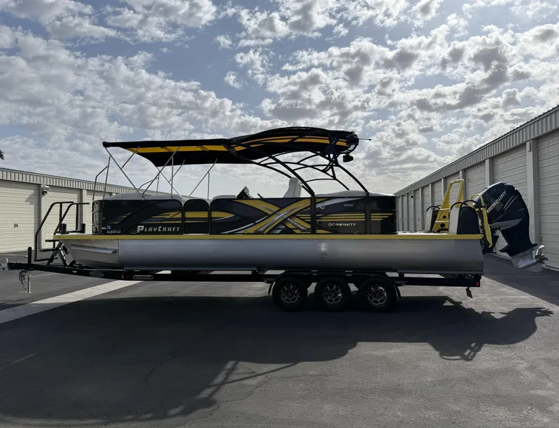 Slide: The Image of 2021 PlayCraft Infinity 2900 pontoon boat with canopy, parked outdoors under a cloudy sky. - 13