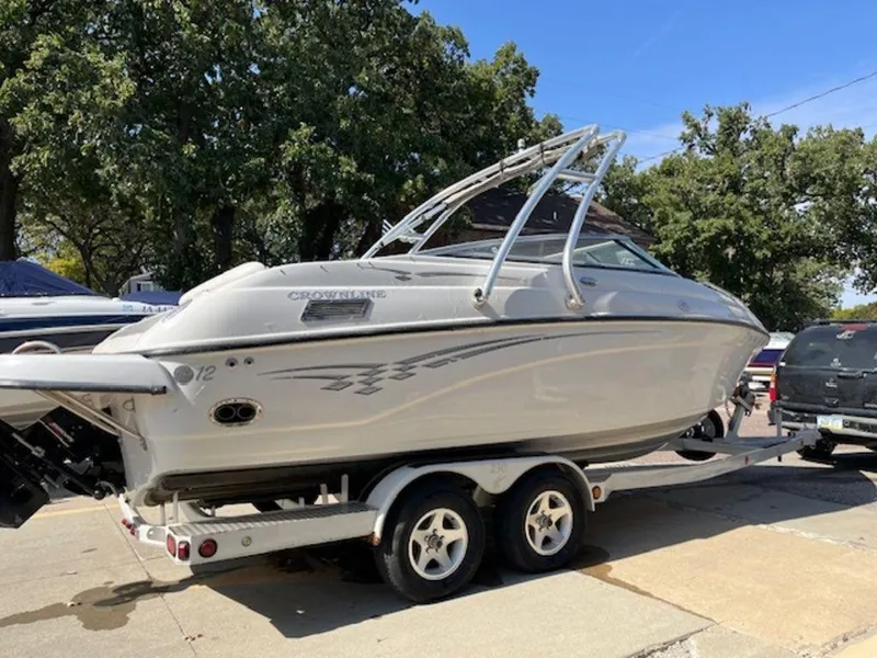 Slide: The Image of 2004 Crownline 230BR boat on trailer, parked outdoors with trees in background. - 2