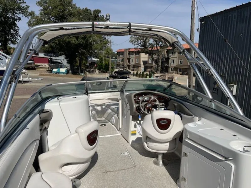 Slide: The Image of 2004 Crownline 230BR boat interior with steering wheel and seating, docked outdoors. - 4