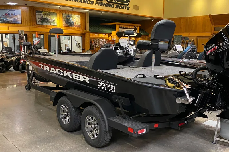 Slide: The Image of 2025 Tracker Savage 215 boat displayed indoors, featuring sleek black design and dual-axle trailer. - 2