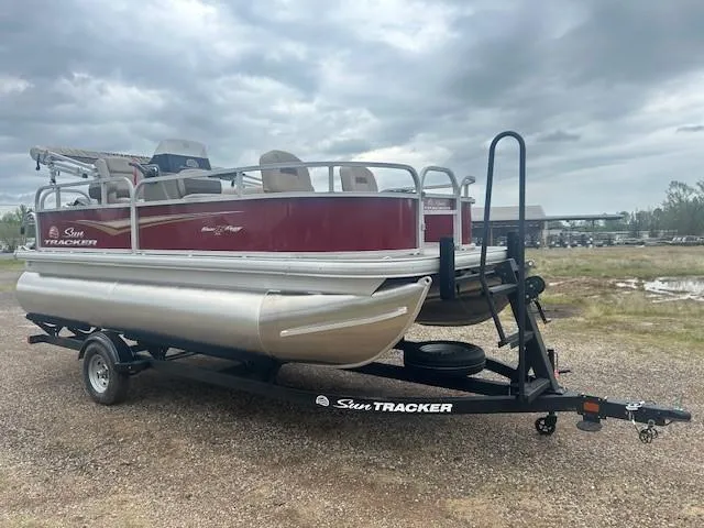 Slide: The Image of 2025 Sun Tracker Bass Buggy 16 XL Select pontoon boat on trailer, parked outdoors. - 3