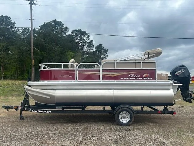 Slide: The Image of 2025 Sun Tracker Bass Buggy 16 XL Select pontoon boat on trailer, parked outdoors. - 9