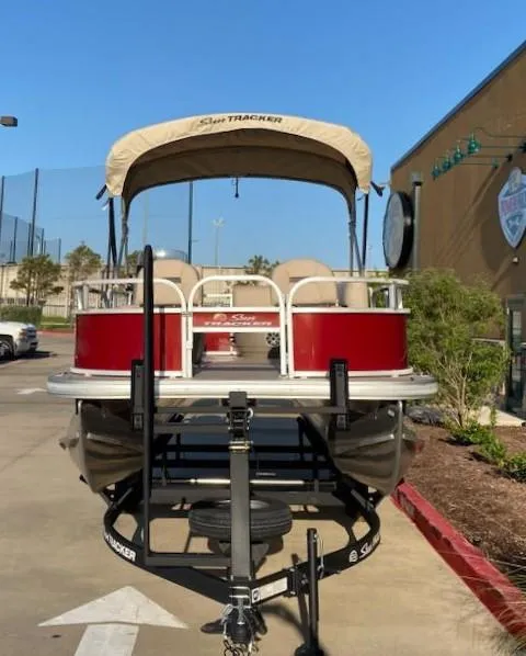 Slide: The Image of 2025 Sun Tracker Bass Buggy 16 XL Select pontoon boat, red and beige, parked outdoors. - 2