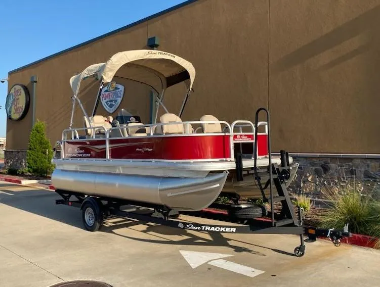 Slide: The Image of 2025 Sun Tracker Bass Buggy 16 XL Select pontoon boat on trailer, parked outdoors. - 4