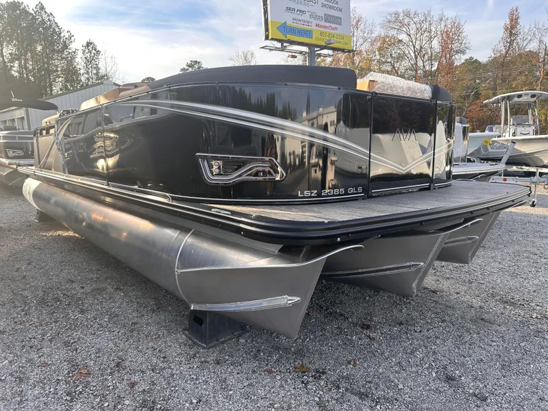 Slide: The Image of 2025 Avalon LSZ Quad Lounger Shift pontoon boat, sleek black design, parked on gravel. - 0