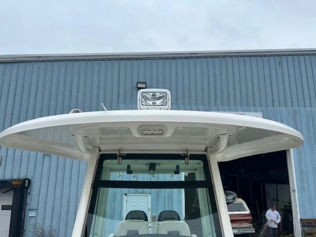 Slide: The Image of 2016 Boston Whaler 250 Outrage boat with hardtop, parked near a blue industrial building. - 14