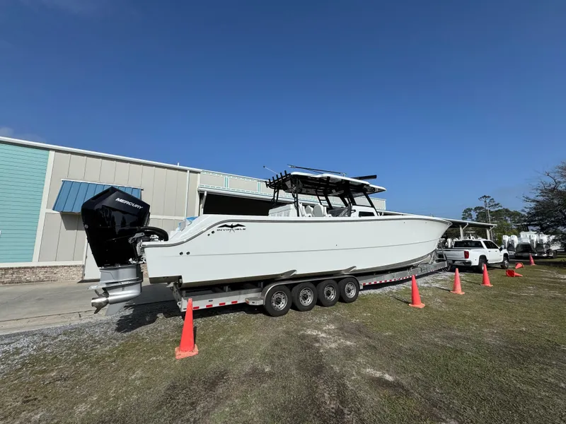 Slide: The Image of 2025 Invincible 46 Catamaran on trailer, parked outdoors near building, with clear blue sky. - 13