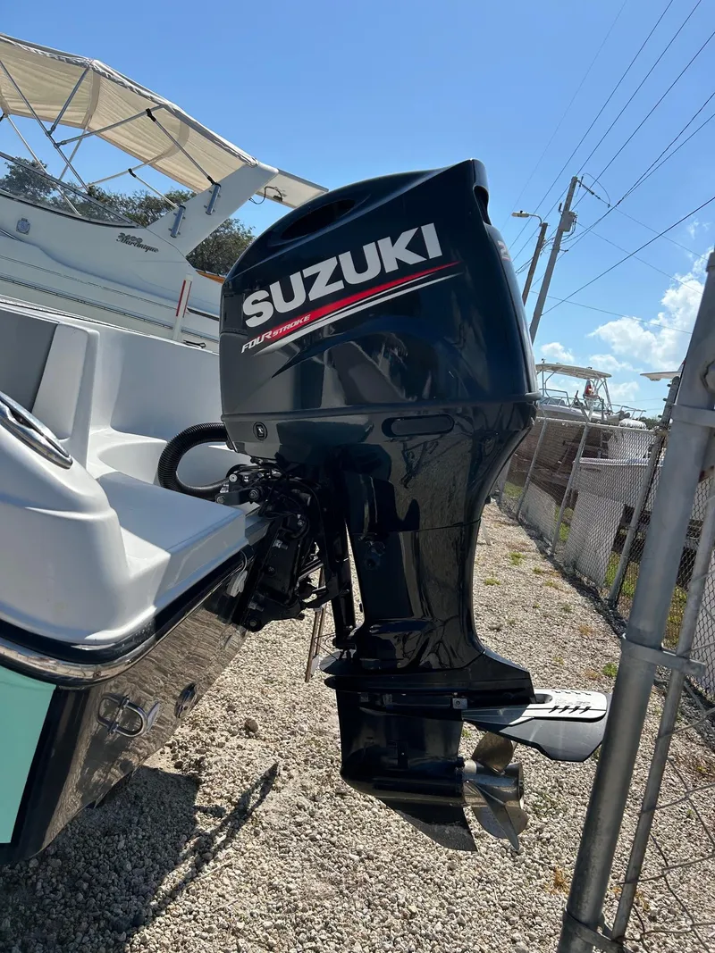 Slide: The Image of 2018 Key Largo 210 boat with Suzuki outboard motor, parked on gravel near a fence. - 5