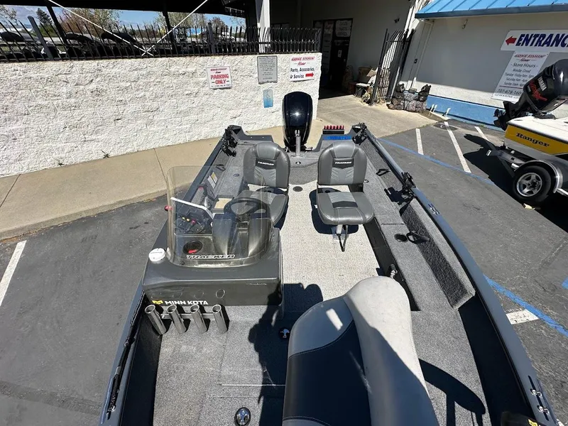 Slide: The Image of 2020 Tracker Pro Guide V-16 SC boat interior with seating and motor, parked outdoors. - 17