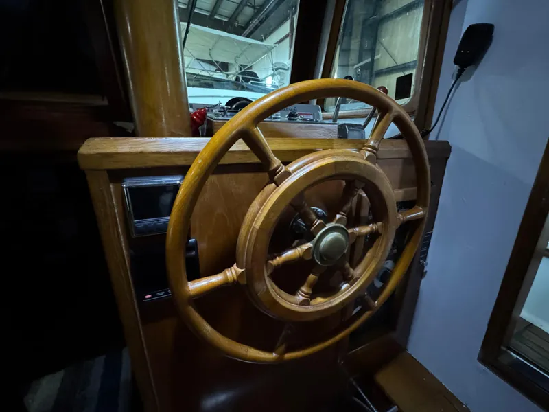 Slide: The Image of Wooden steering wheel of a 1983 Marine Trader 44 Sundeck yacht in a dimly lit cabin. - 10