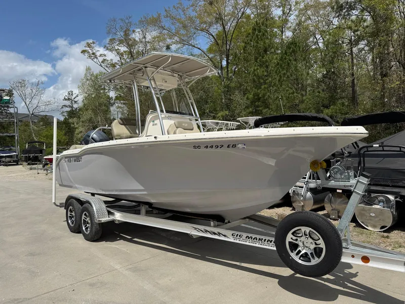 Slide: The Image of 2022 Key West 219 FS boat on trailer, parked outdoors, surrounded by trees and clear sky. - 0