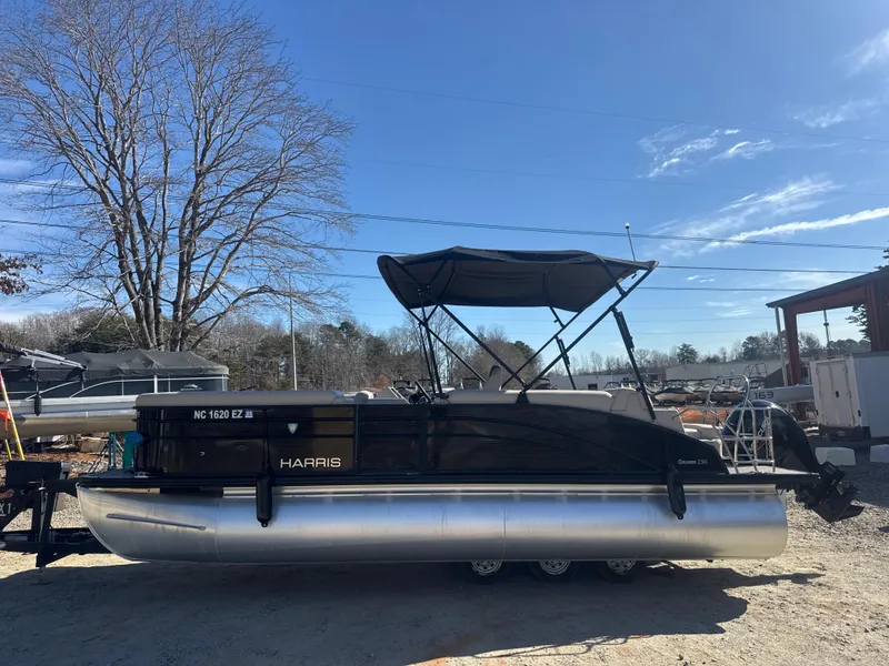 Slide: The Image of 2023 Harris HCX230 SL pontoon boat with canopy, parked outdoors under clear blue sky. - 1