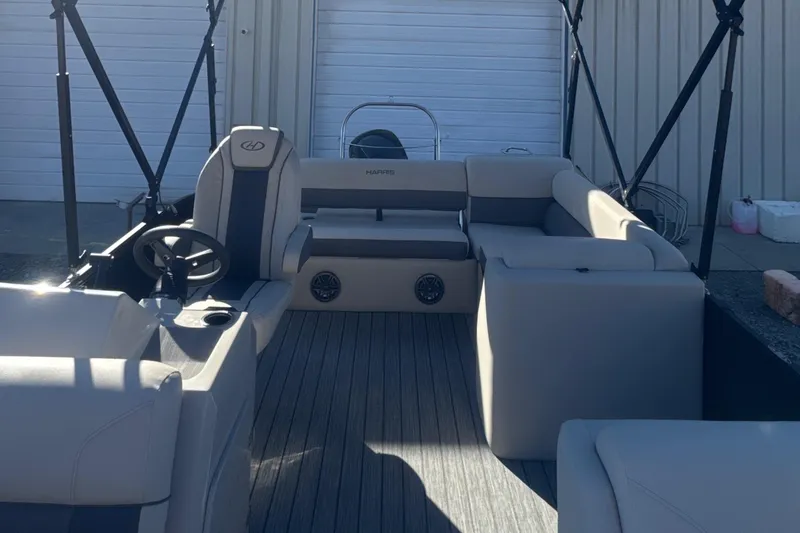 Slide: The Image of 2023 Harris HCX230 SL pontoon boat interior with seating and steering wheel, docked near a building. - 17
