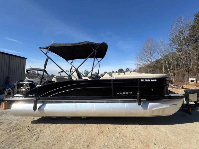 Slide: The Image of 2023 Harris HCX230 SL pontoon boat with black canopy, parked outdoors on a sunny day. - 8