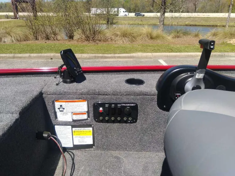 Slide: The Image of 2025 Tracker Panfish 17 boat interior with control panel and seat, parked near a pond. - 8