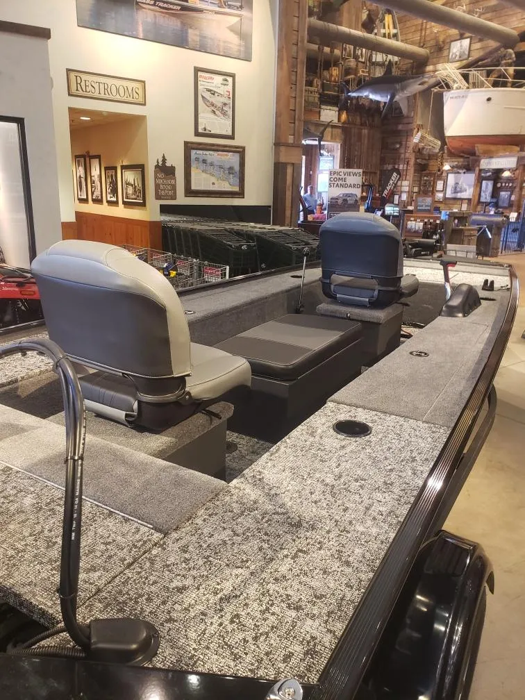 Slide: The Image of 2025 Tracker Panfish 17 boat interior in showroom, featuring seating and fishing setup. - 2
