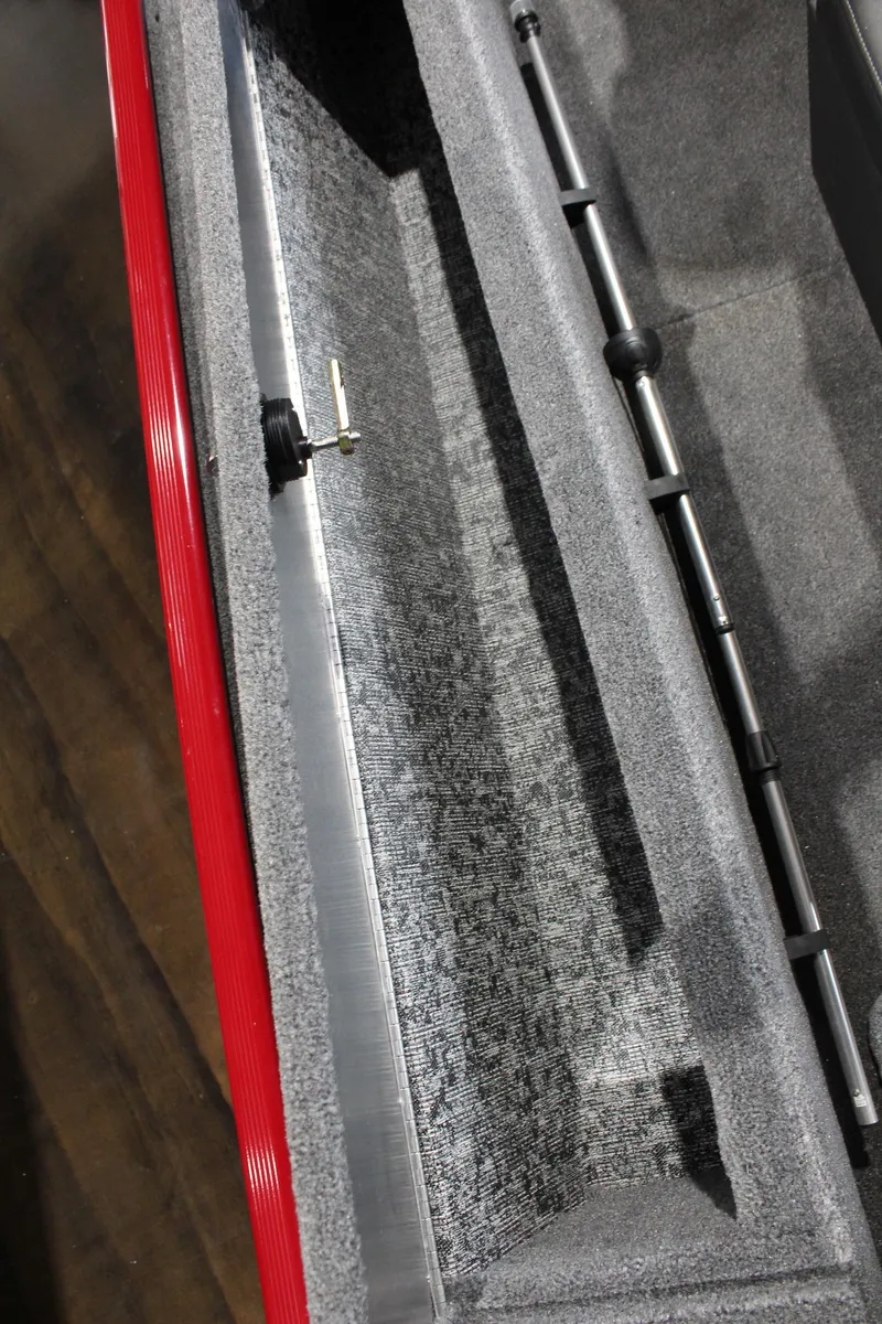 Slide: The Image of 2025 Tracker Panfish 17 boat interior storage compartment with red trim and rod holders. - 14